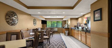A hotel dining area with booths and tables, a patterned carpet, and a view of greenery outside.