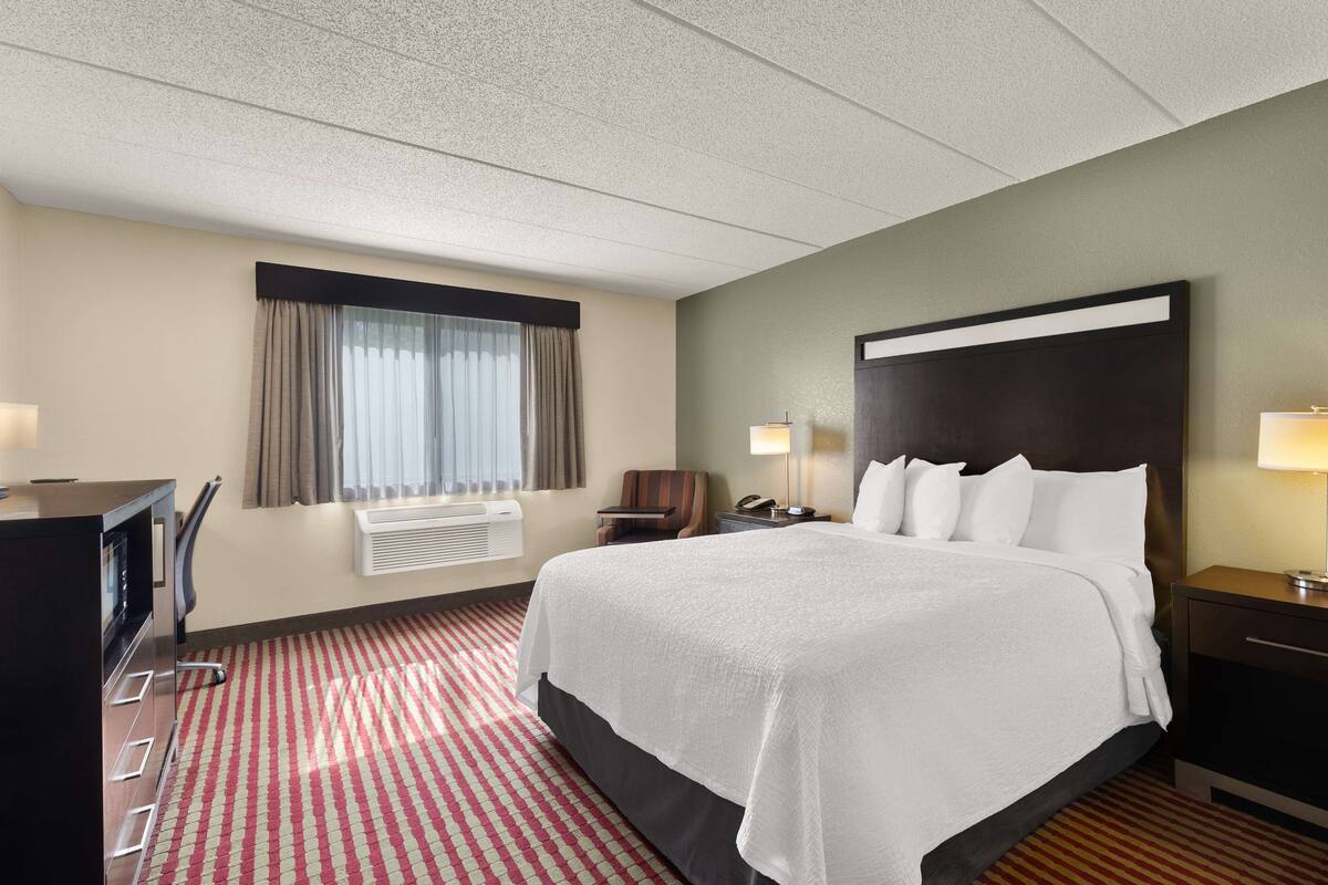 A hotel room with a large bed, a desk, a chair, a TV, and a window with curtains.