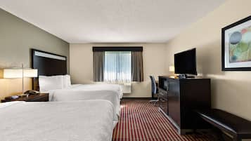 A hotel room with two beds, a desk with a TV, a lamp, and a bench.
