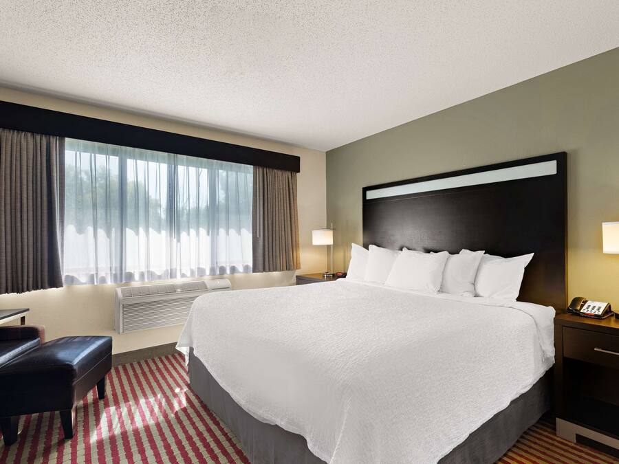 Habitación de hotel con una cama grande, un escritorio, una silla, una lámpara y una ventana con cortinas.