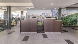 A hotel lobby with a reception desk, seating area, and a cityscape mural on the wall. - La Quinta Inn & Suites by Wyndham Kansas City Airport (Kansas City)