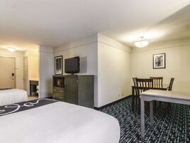 Habitación de hotel con dos camas, un escritorio, una silla, un televisor y un microondas.