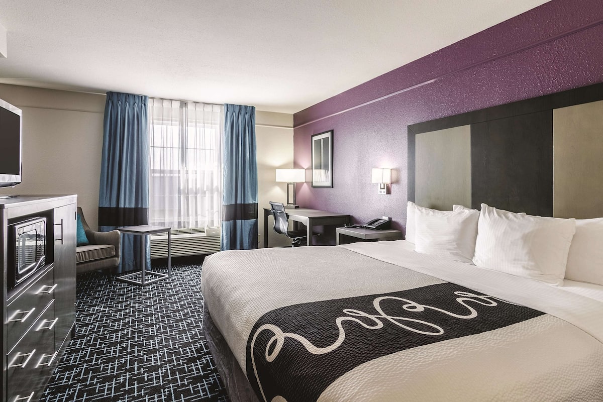 A hotel room with a bed, a desk, a chair, a television, and a window with curtains.
