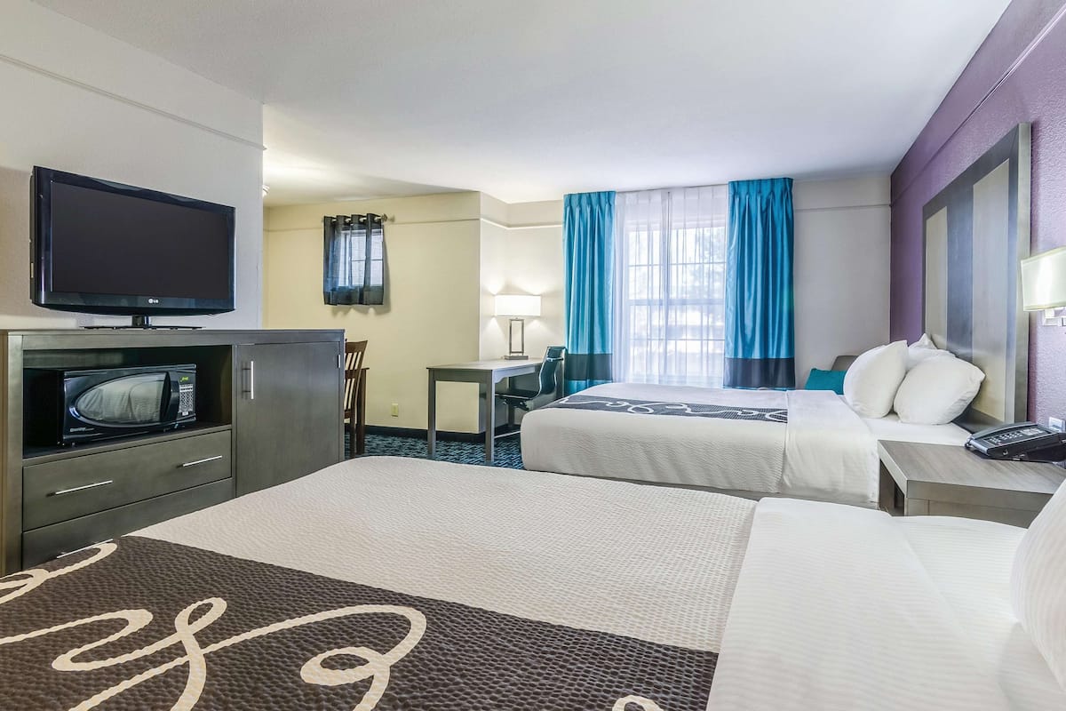 A hotel room with two beds, a TV, a desk, and a chair.