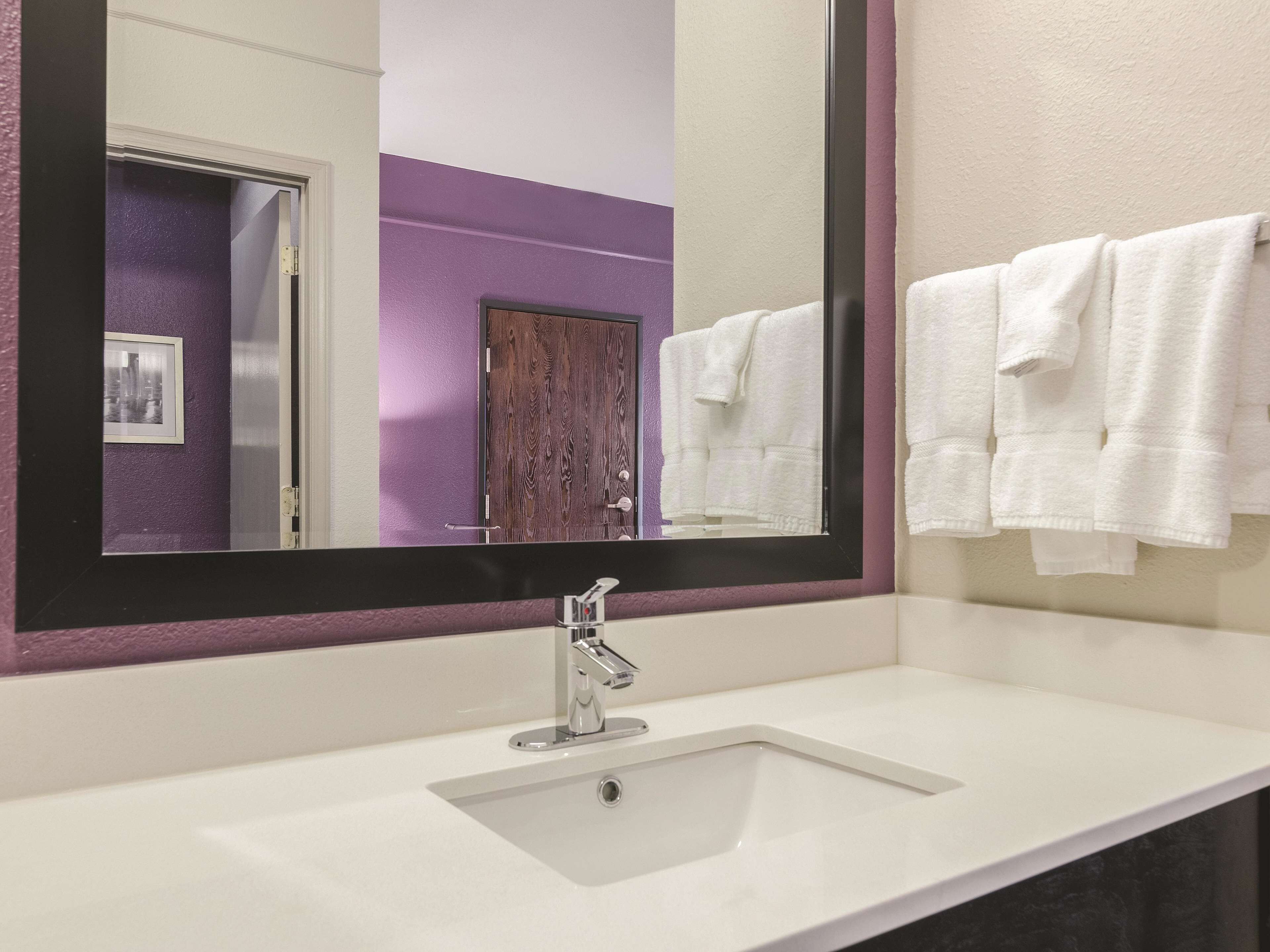 Un baño con un lavamanos blanco, un espejo grande y una pared morada.