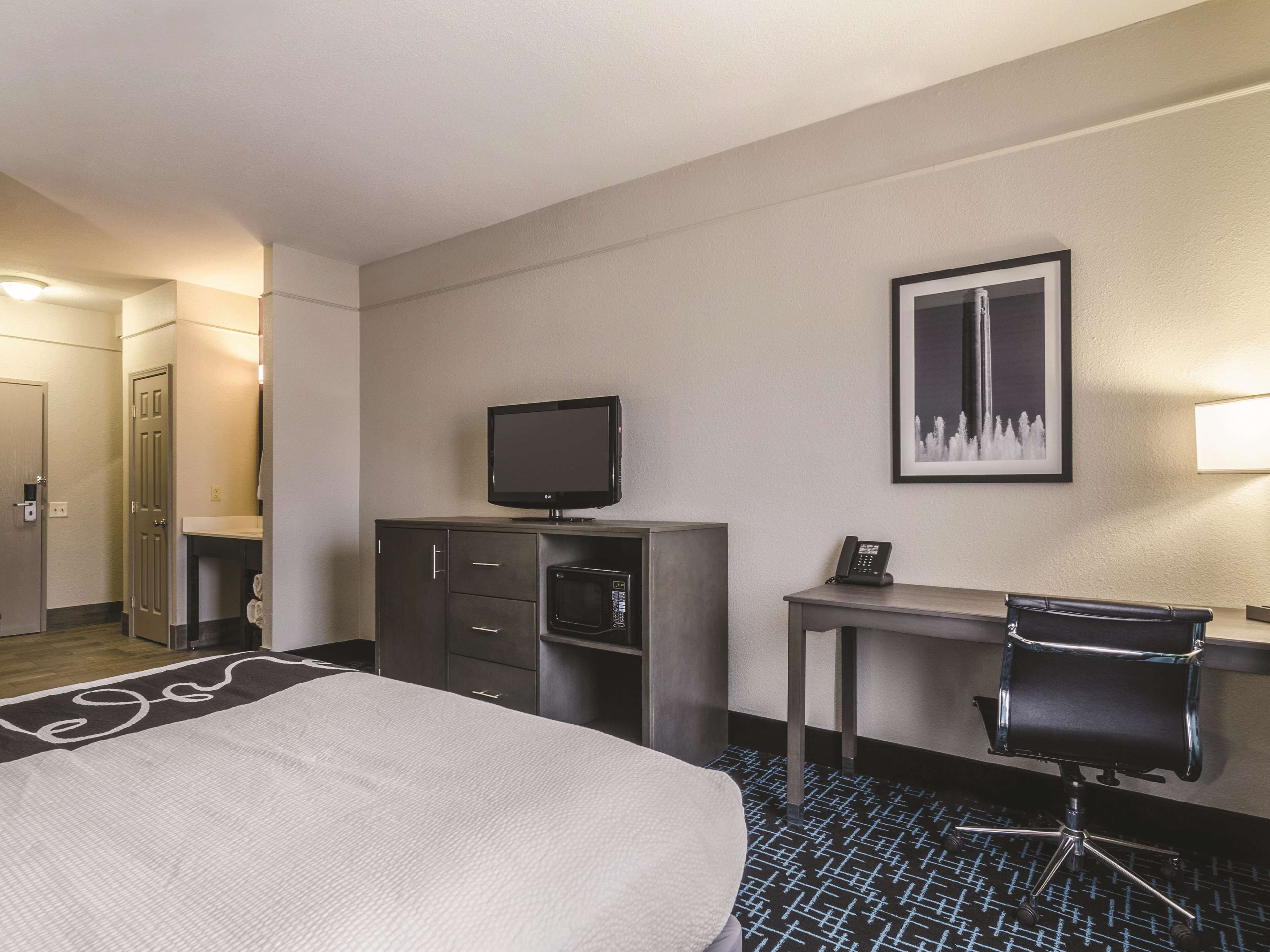 Una habitación de hotel con cama, escritorio, silla, televisión, teléfono y un cuadro en la pared.