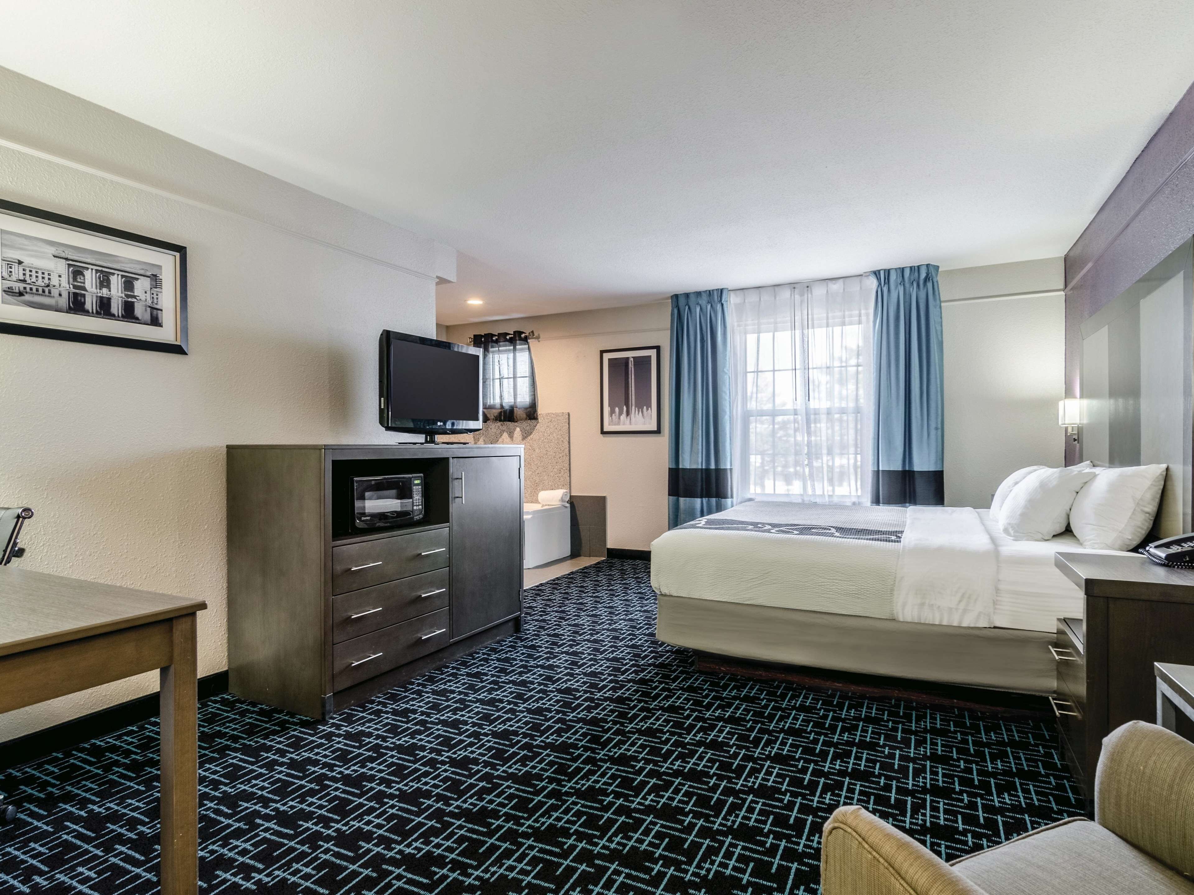 A hotel room with a bed, a desk, a television, a microwave, and a bathroom.