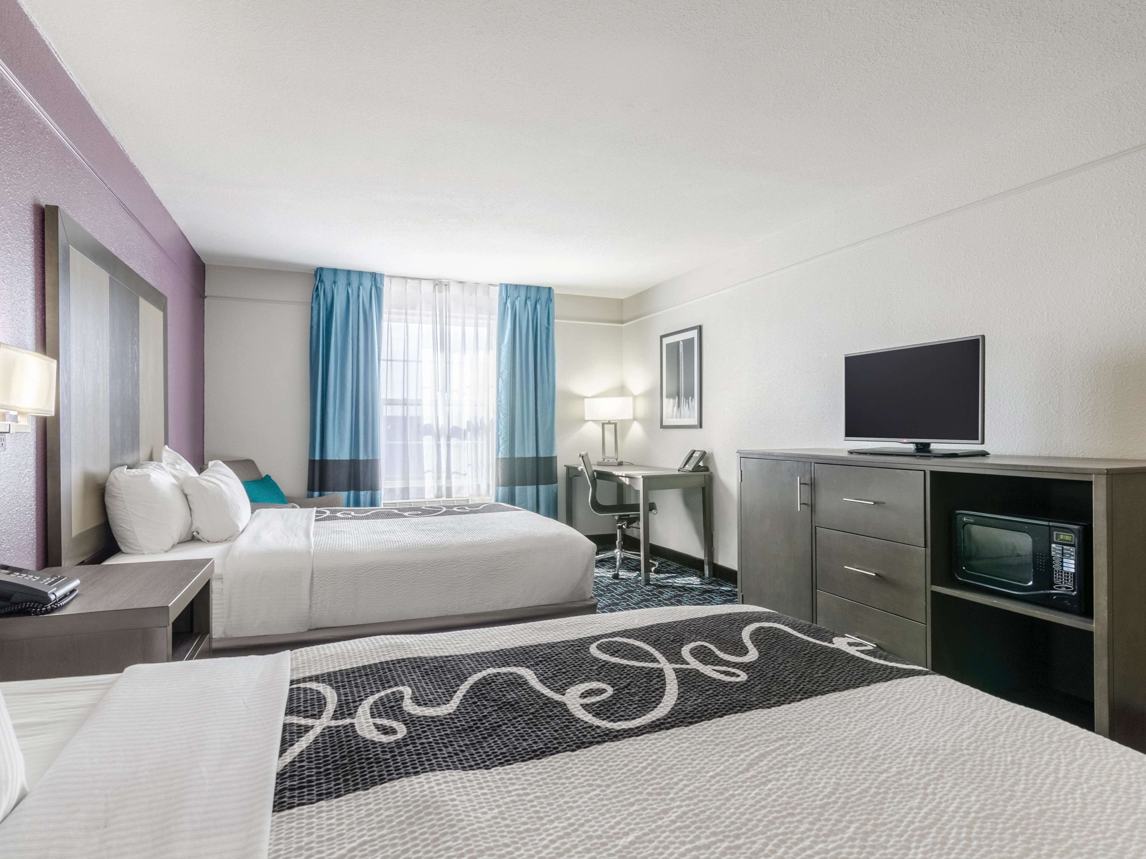 A hotel room with two beds, a desk with a chair, a television, and a microwave.