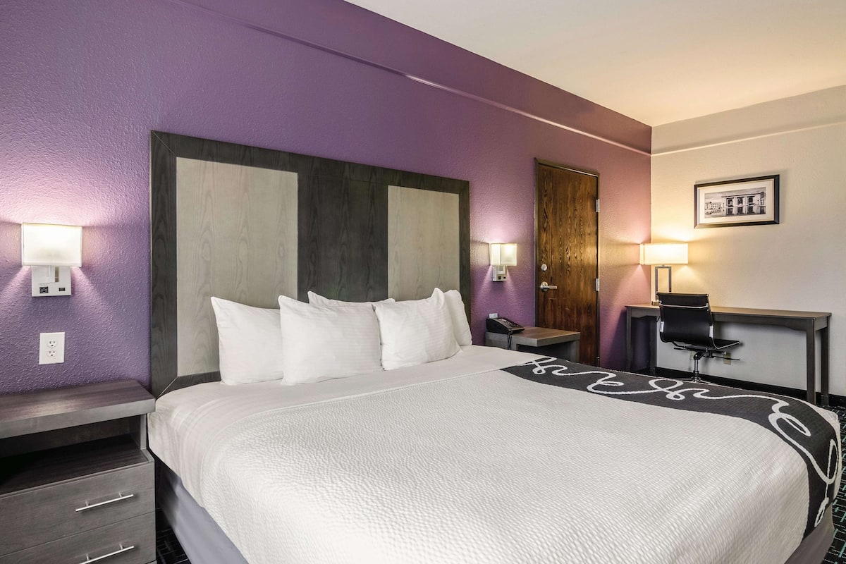 A hotel room with a large bed, a desk, and two wall-mounted lamps.