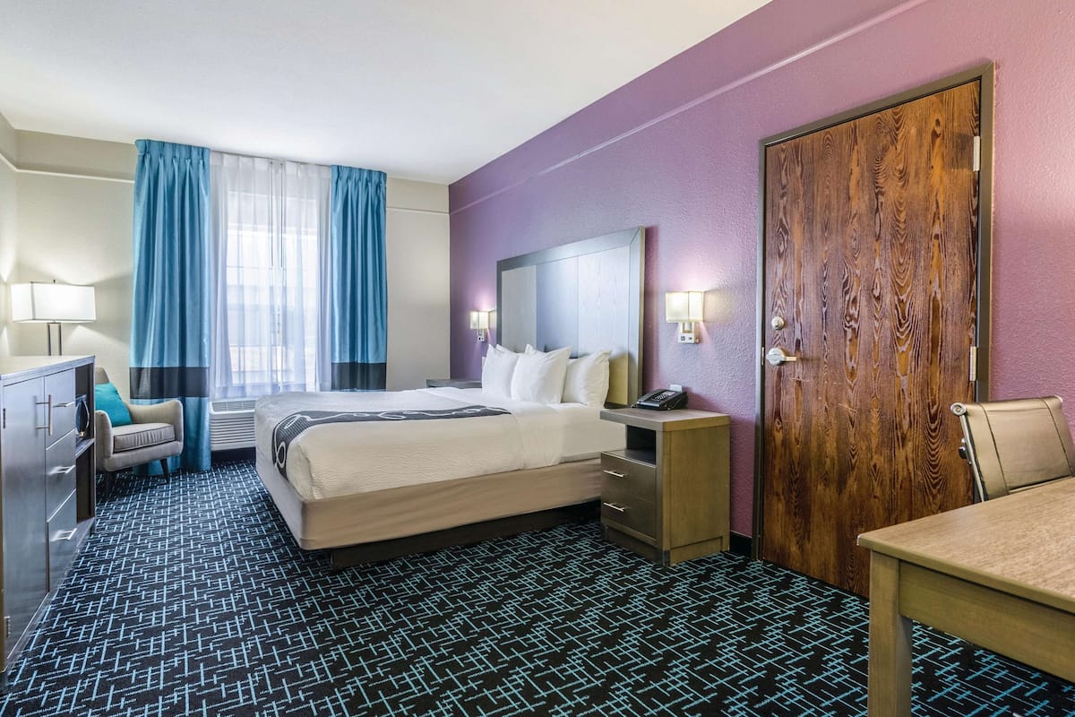 A hotel room with a bed, bedside table, lamp, and a wooden door.