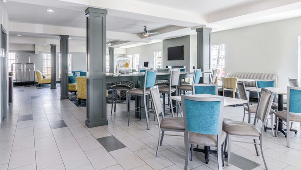 A modern dining area with high tables and chairs, a flat-screen TV mounted on the wall, and a seating area with cushioned benches. - La Quinta Inn & Suites by Wyndham Kansas City Airport (Kansas City)