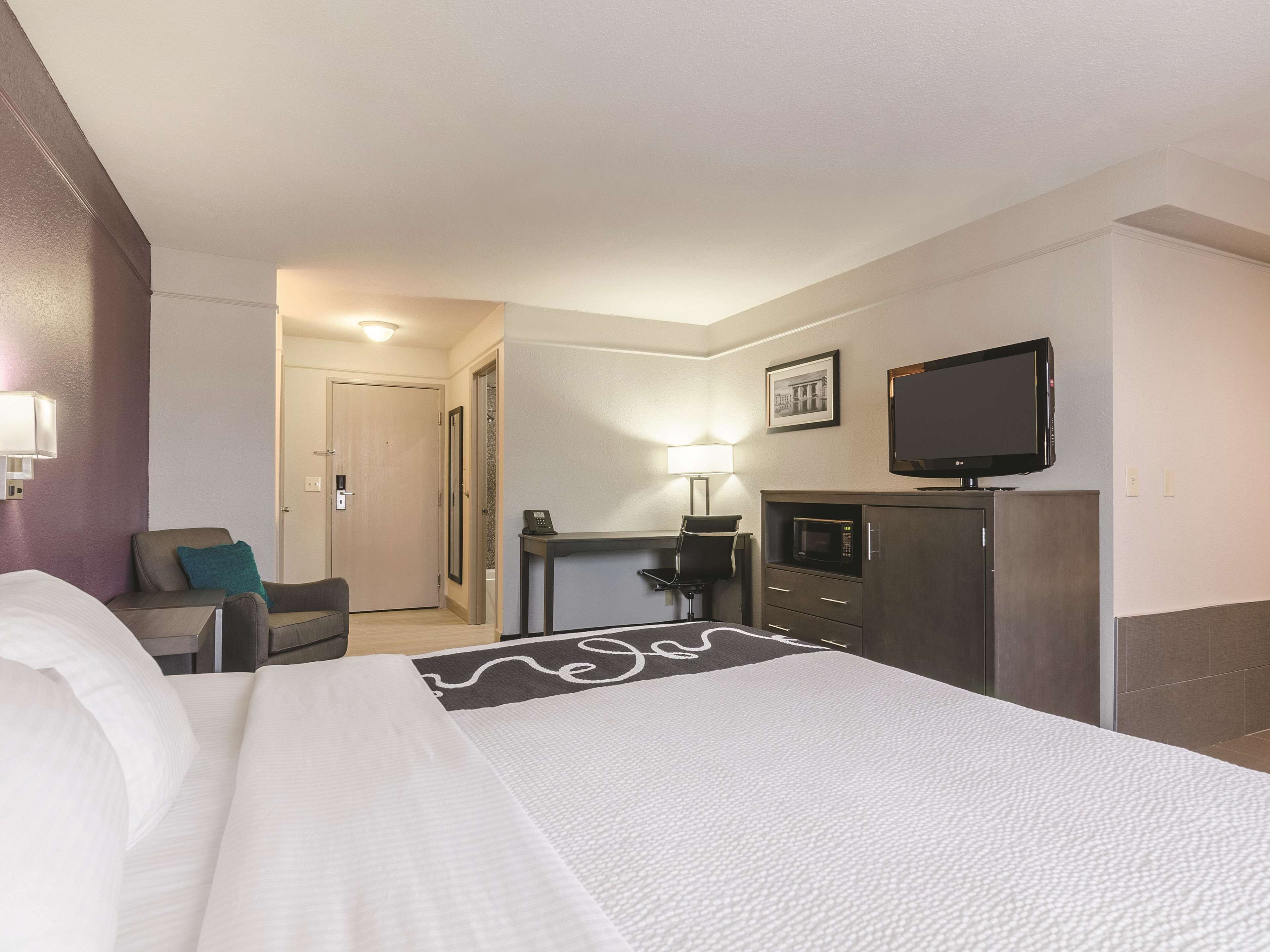 Habitación de hotel con cama, escritorio, silla, televisor, microondas y puerta.