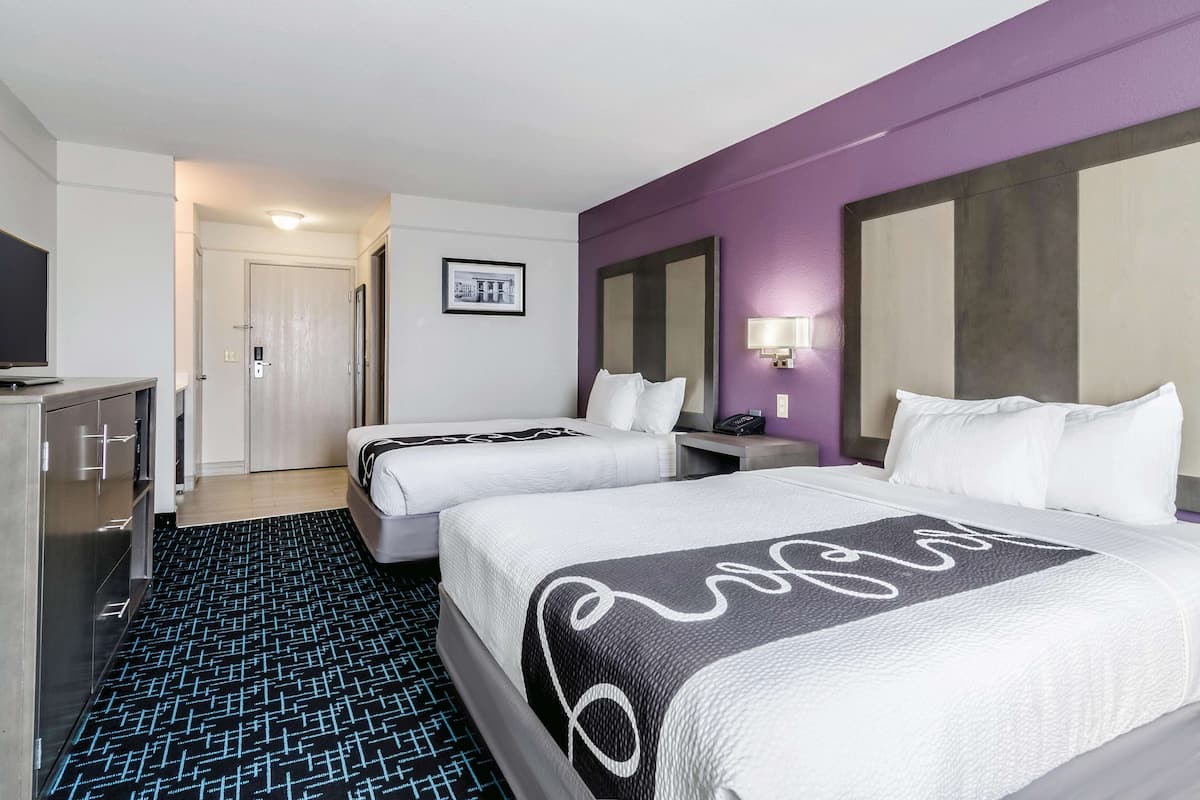 A hotel room with two beds, a desk, a TV, and a bathroom door.