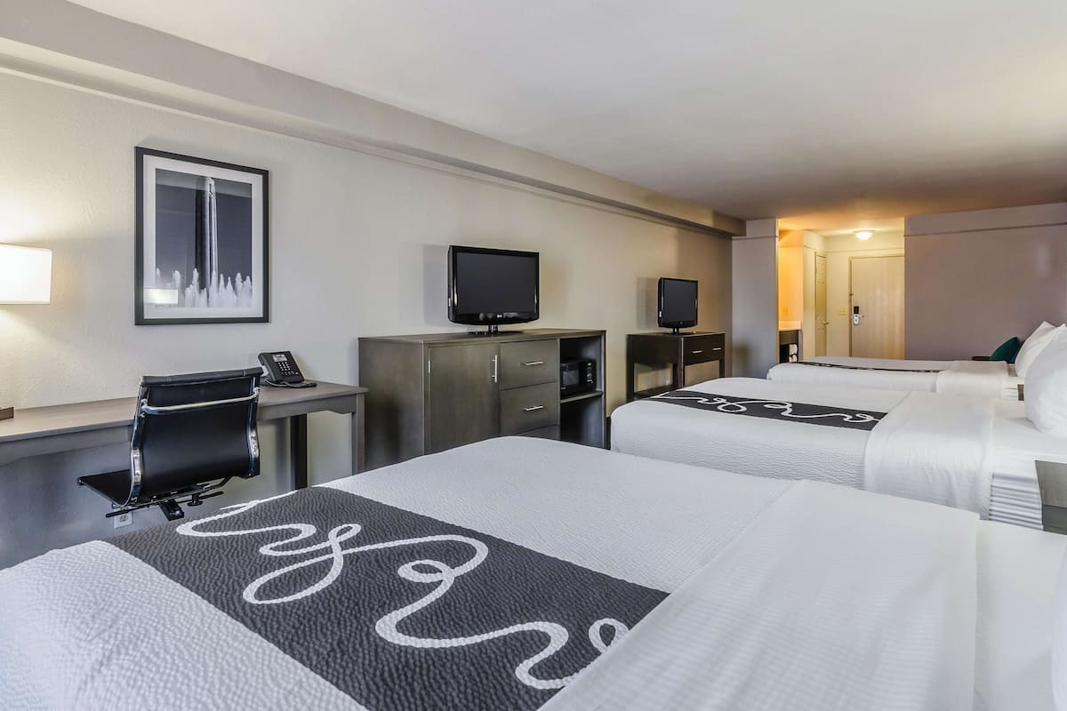 A hotel room with two beds, a desk with a computer and phone, a television, and a framed picture on the wall.