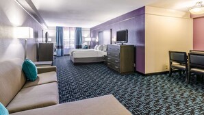 A hotel room with a bed, a sofa, a desk, a TV, and a dresser. - La Quinta Inn & Suites by Wyndham Kansas City Airport (Kansas City)