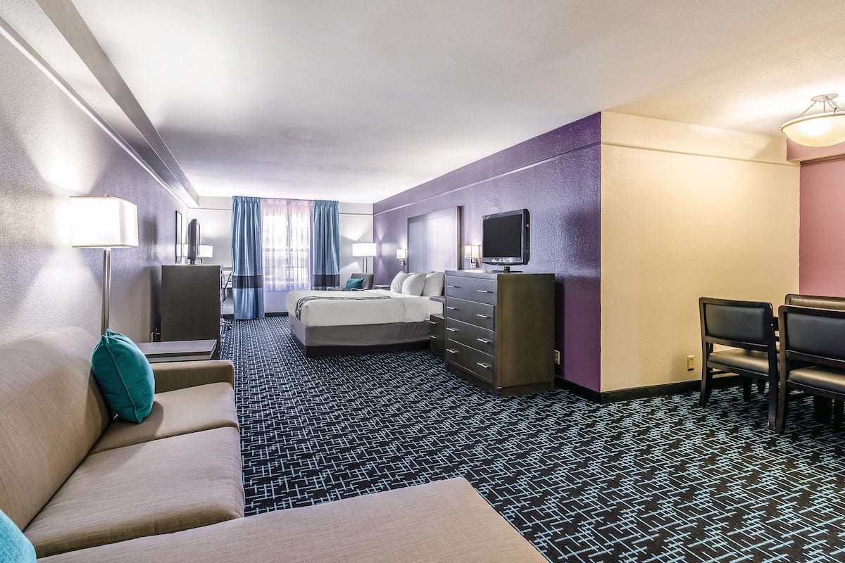 A hotel room with a bed, a sofa, a desk, a TV, and a dresser.