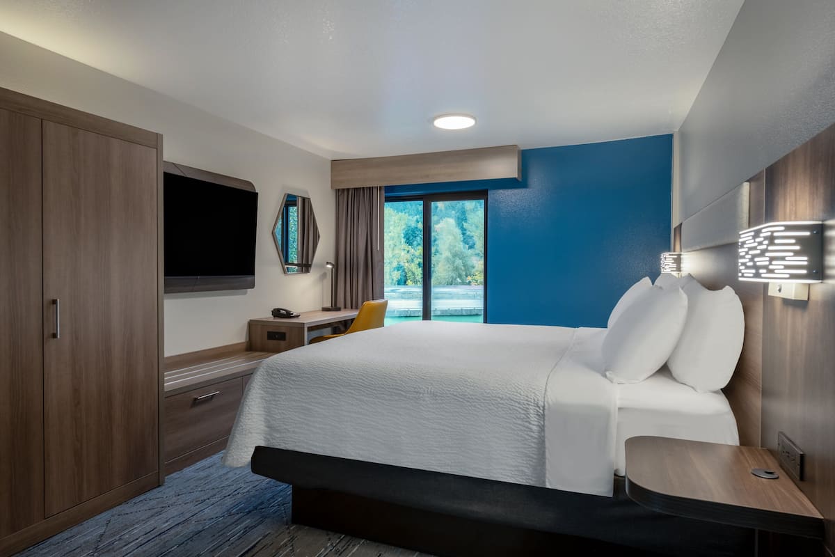 A modern hotel room with a large bed, a desk, a TV, and a view of the outdoors.
