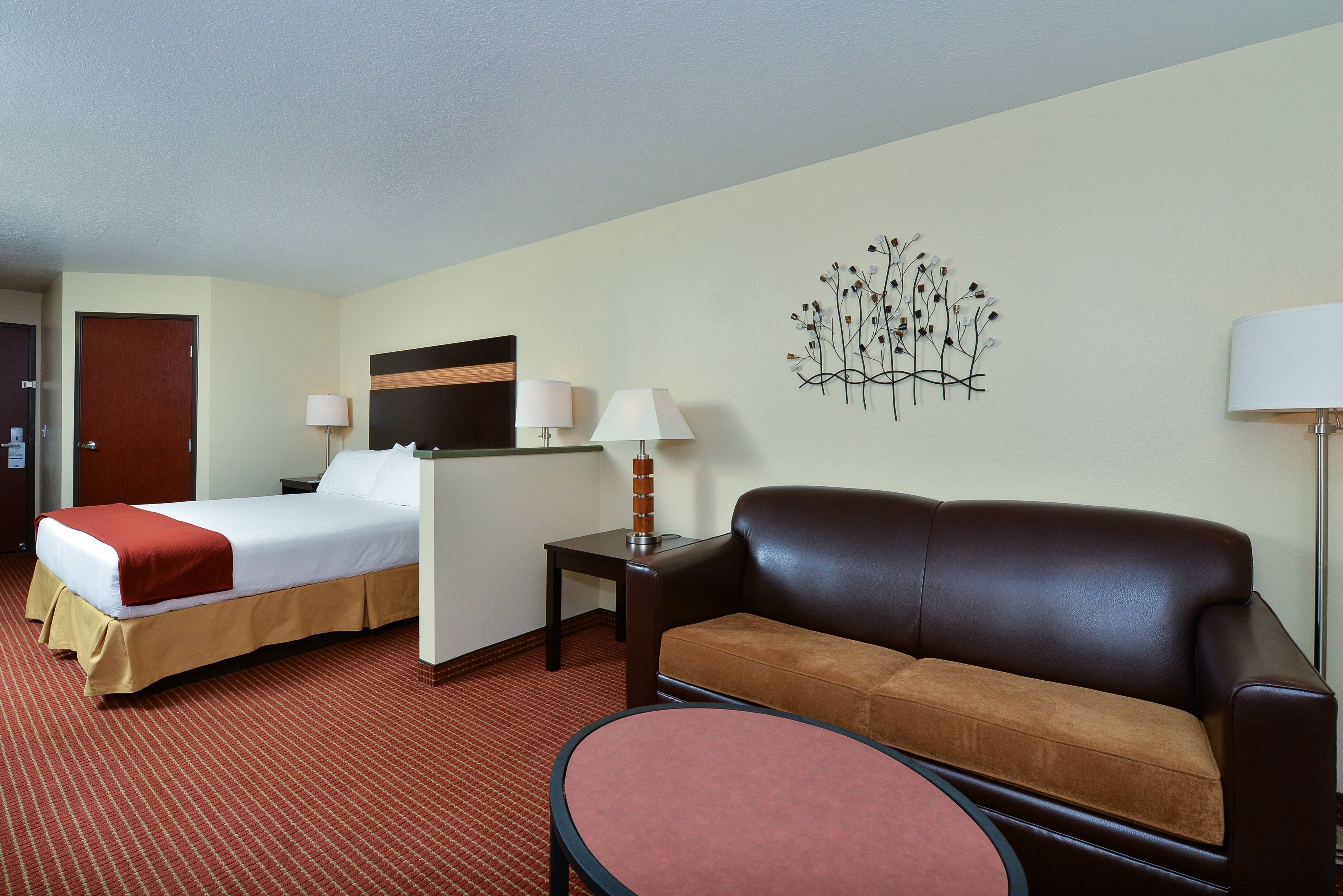 A hotel room with a bed, a sofa, a small table, and a wall-mounted lamp.