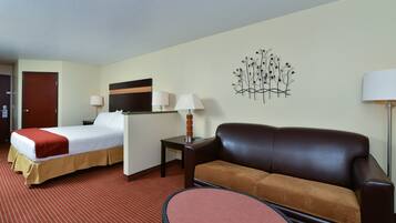 A hotel room with a bed, a sofa, a small table, and a wall-mounted lamp.