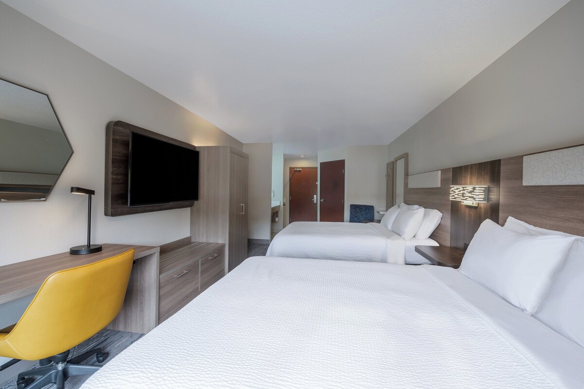 Een hotelkamer met twee bedden, een bureau met stoel, een televisie en een spiegel.