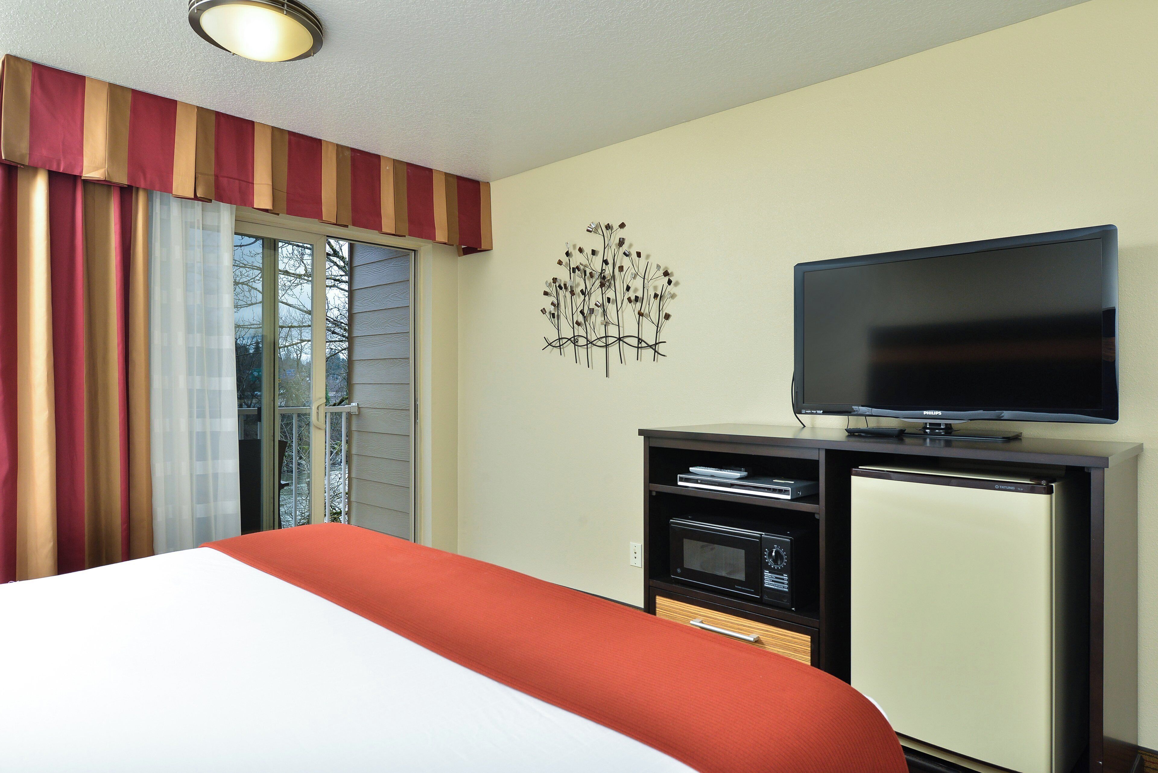 Una habitación de hotel con cama, televisión, minibar y un adorno en la pared.