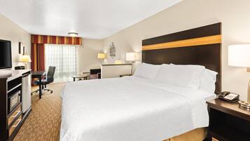 A hotel room with a large bed, a desk with a chair, a television, and a minibar.