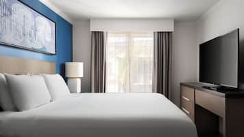 Una habitación de hotel con una cama grande, televisor, escritorio y ventana con cortinas.