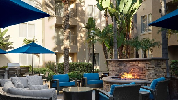 An outdoor patio with wicker furniture, a stone fire pit, and blue umbrellas. - HYATT house San Diego/Sorrento Mesa (San Diego)