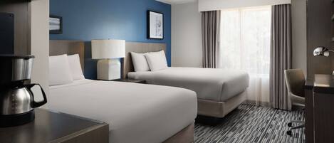 A hotel room with two beds, a desk with a coffee maker, a lamp, and a chair.