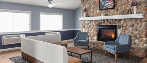 A living room with a stone fireplace, a ceiling fan, and a large window.