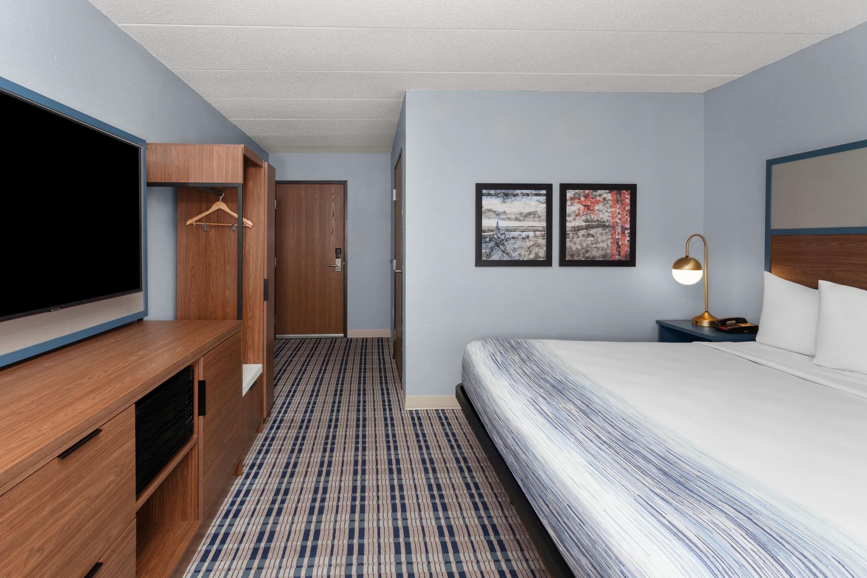 Ein Hotelzimmer mit einem Bett, einem Fernseher, einem Holzschrank und zwei gerahmten Bildern an der Wand.