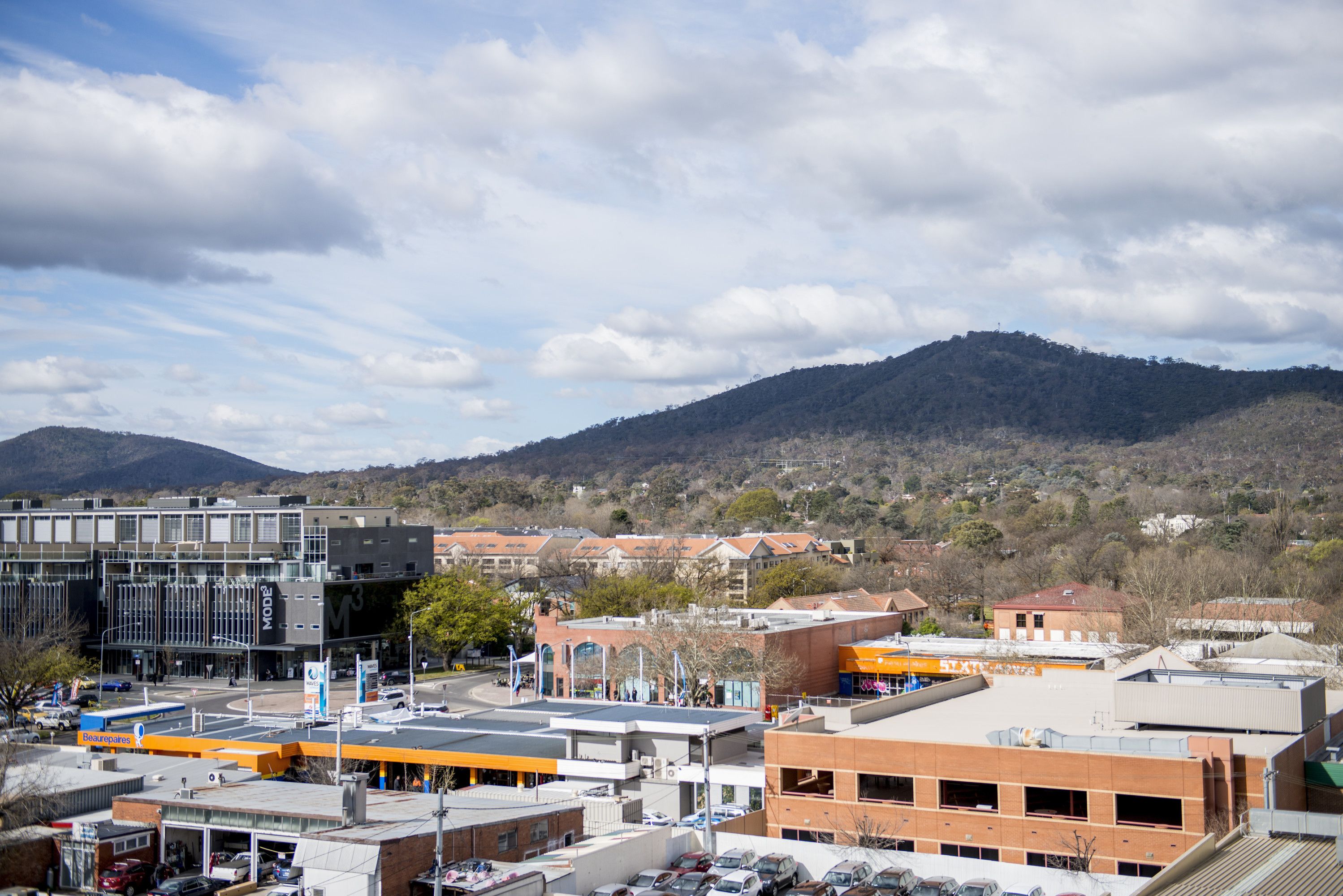 Une zone commerciale dotée d’un parking, de bâtiments et bordée par un paysage montagneux.