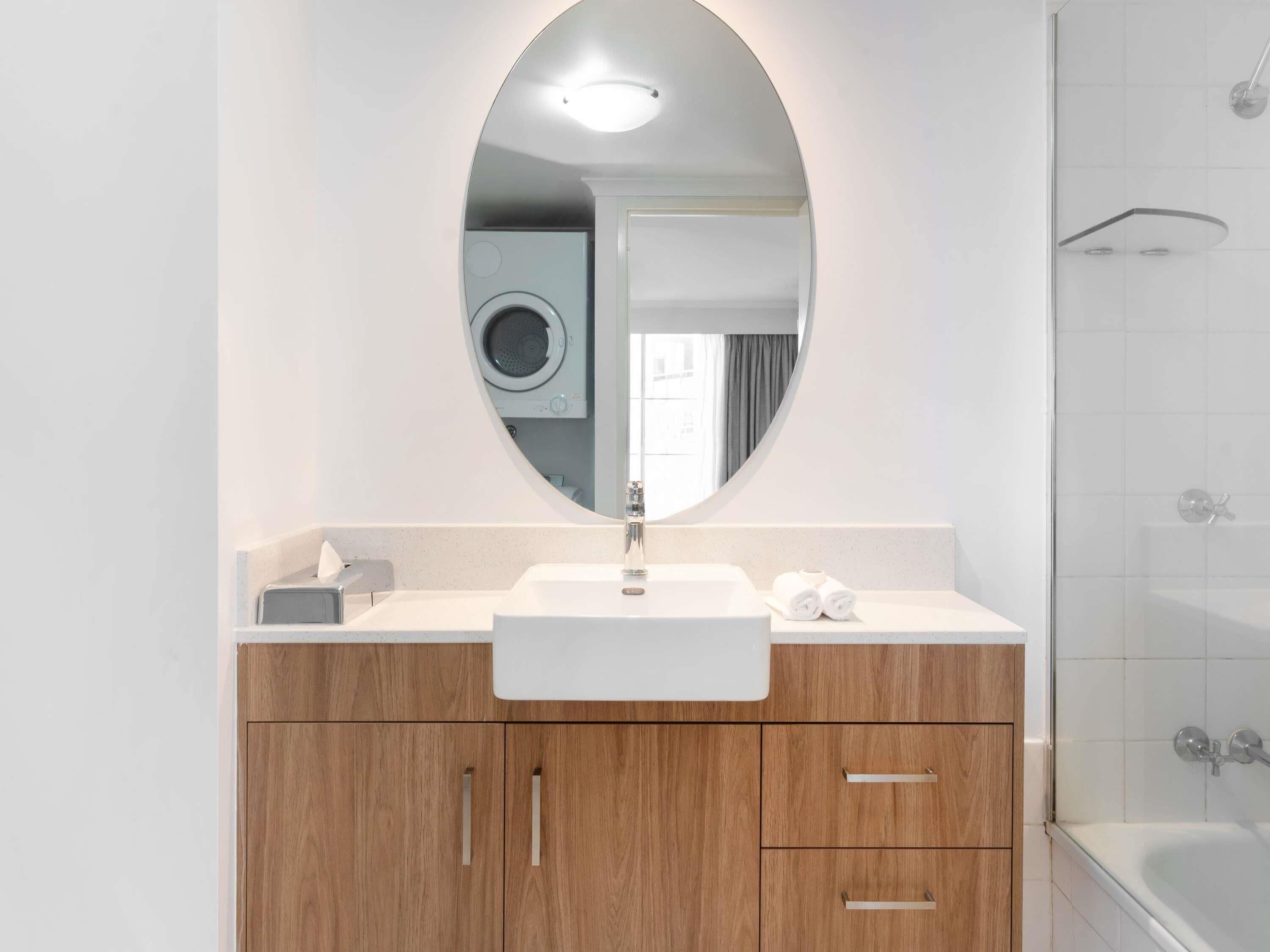 Een moderne badkamer met een ronde spiegel, een wastafel, houten kastjes en een douchehoek.