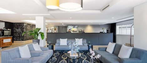 A modern hotel lobby with seating areas, a reception desk, and a bar.