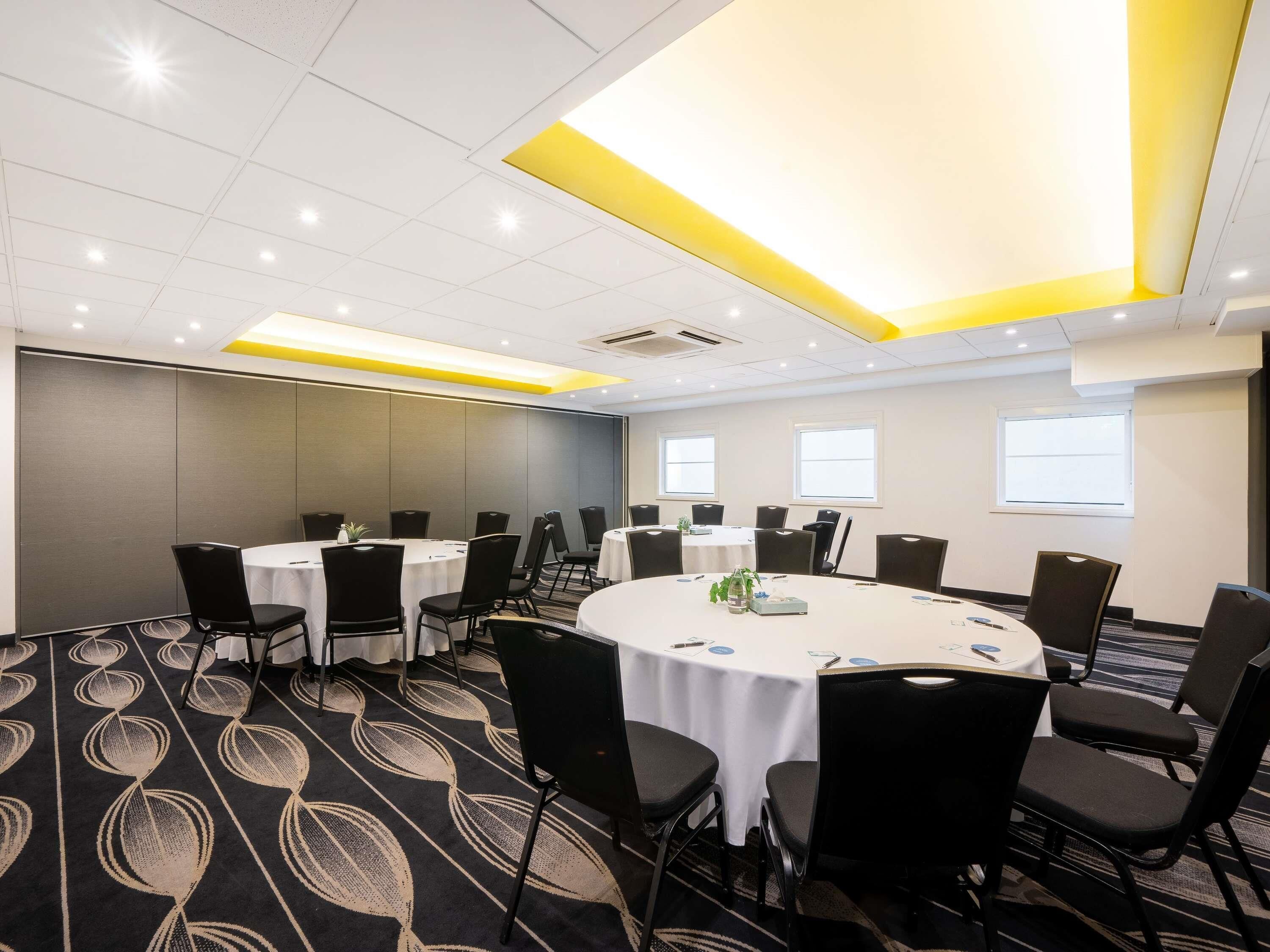 Une salle de conférence avec des tables rondes, des chaises noires et un tapis à motifs.