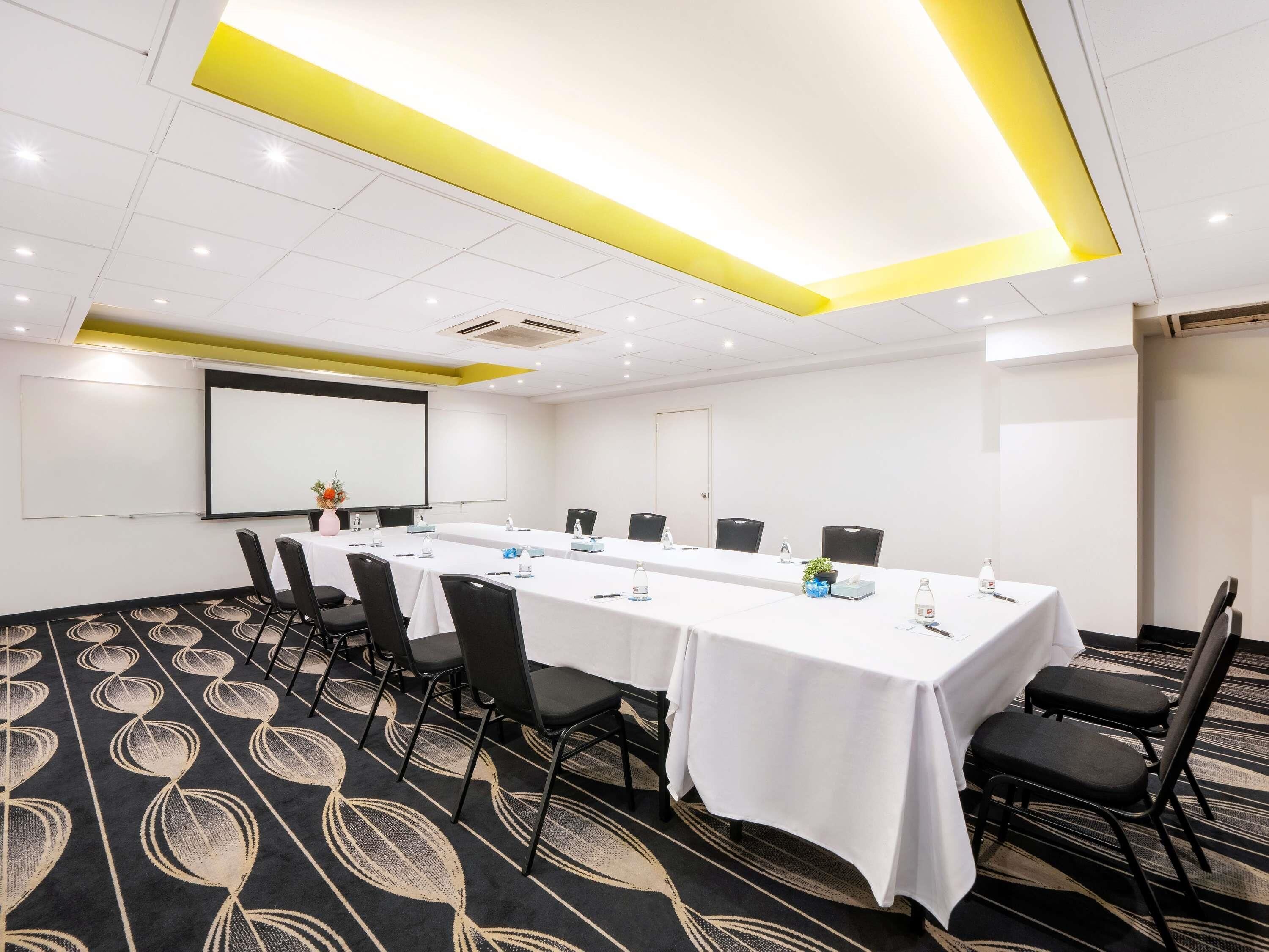 Una sala de conferencias con una mesa larga, sillas, una pantalla de proyector y una pizarra.
