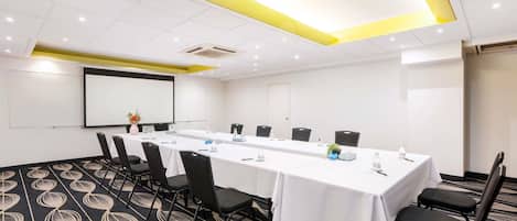 Una sala de conferencias con una mesa larga, sillas, una pantalla de proyector y una pizarra.