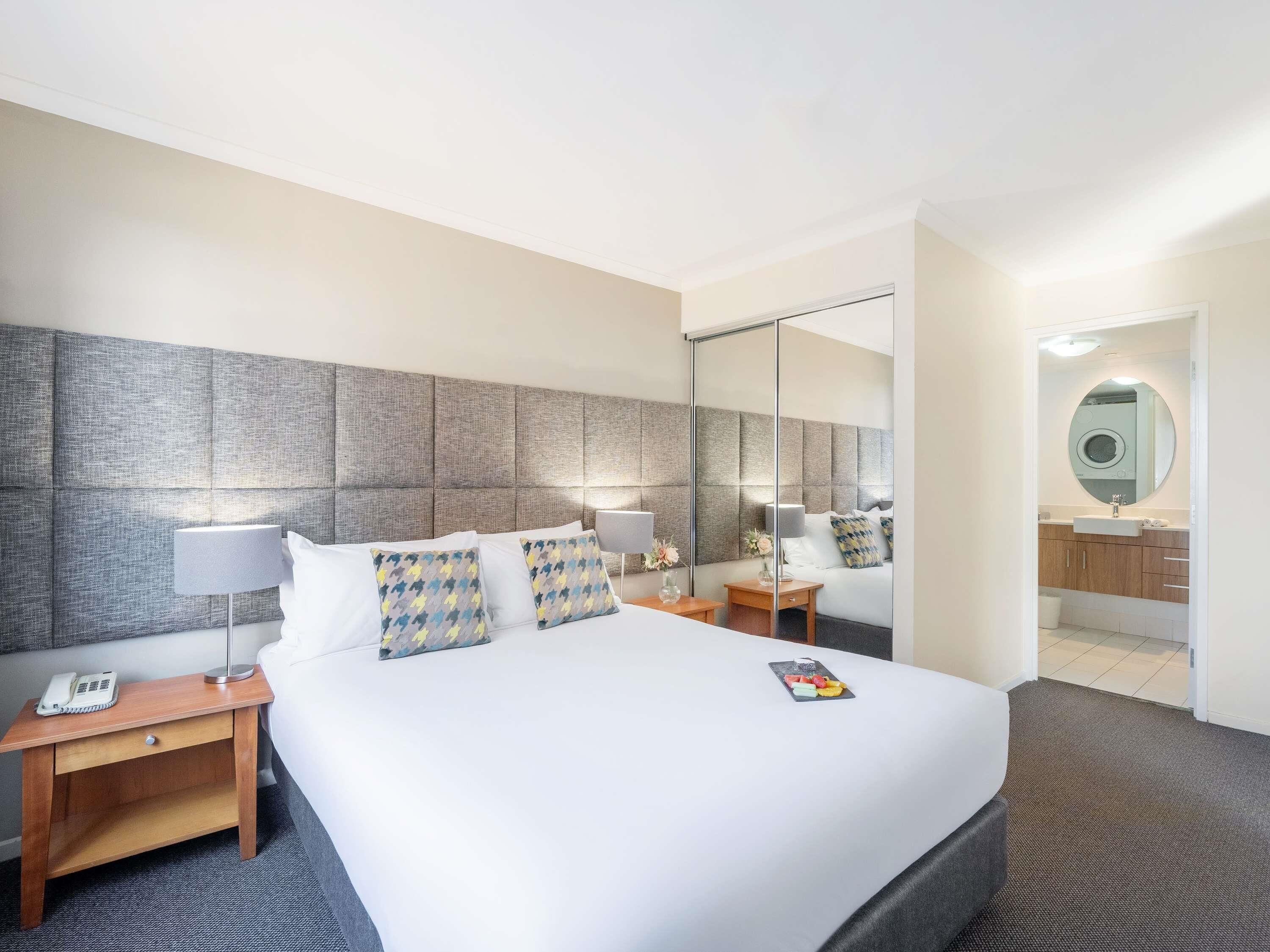 Una camera d'albergo con un letto grande, comodini, uno specchio e un bagno visibile attraverso una porta aperta.