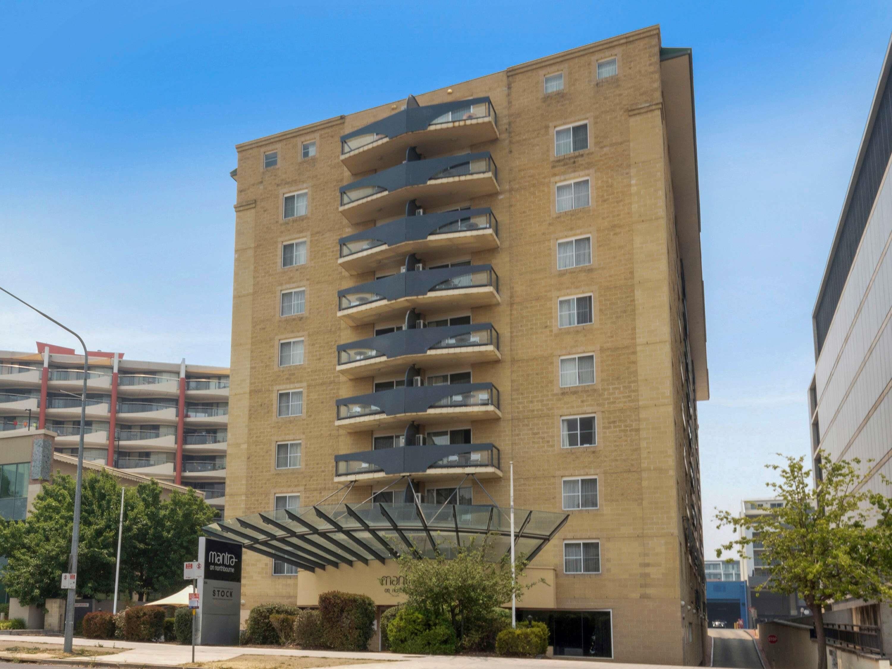 Een meerlaags gebouw met balkons, een overdekte ingang en een bord met 'Mantra on Northbourne'.