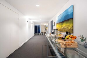 Stunning hotel corridor with a carpeted floor and white walls, leading to a reception area with a display case and a large painting.