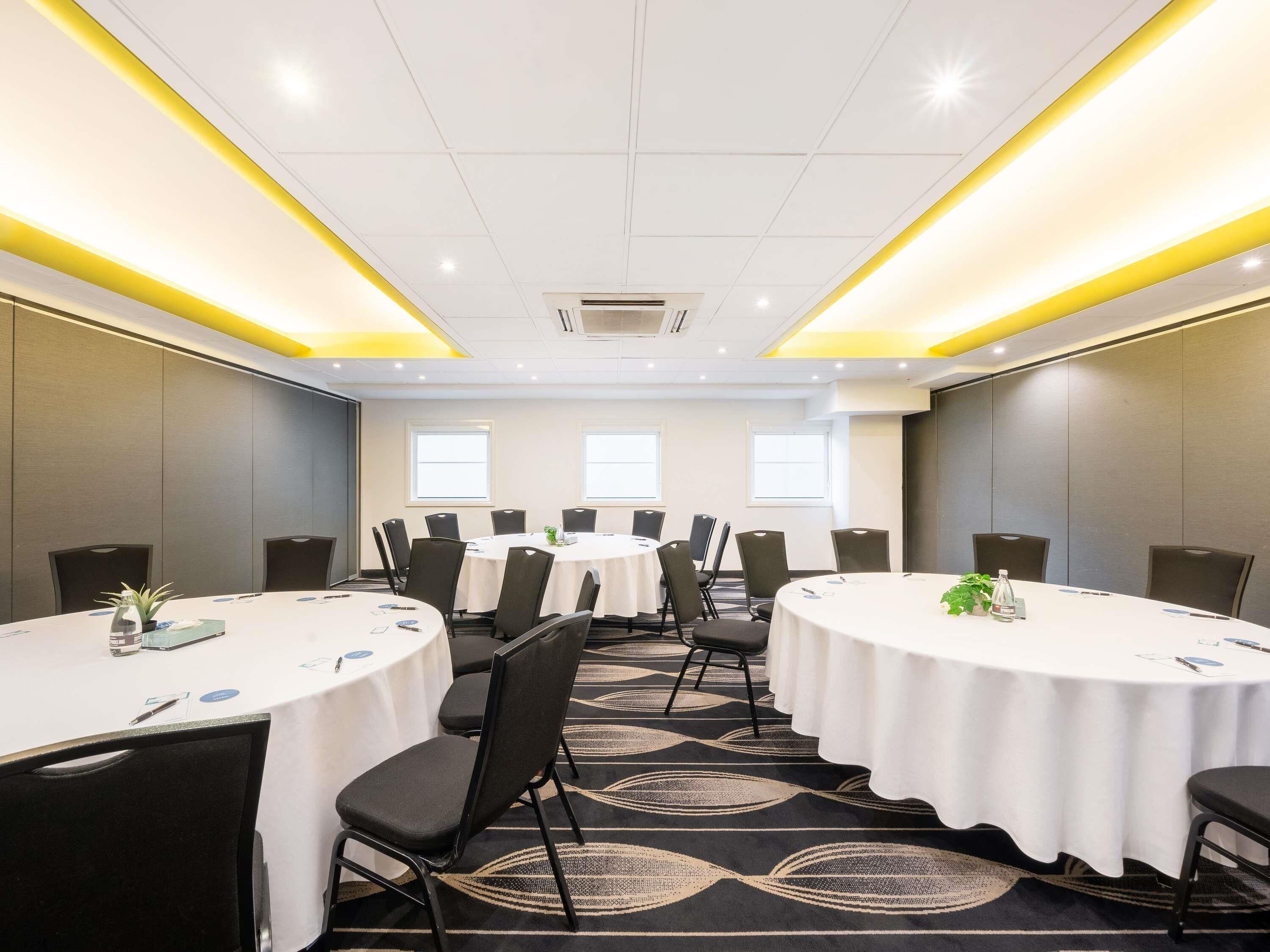 Un salón de conferencias con mesas redondas, sillas y piso alfombrado.