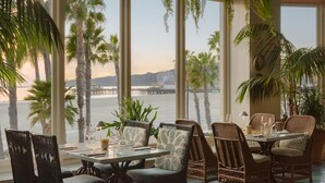 Un comedor con mobiliario de mimbre, ventanas amplias y vistas a la playa y al muelle.