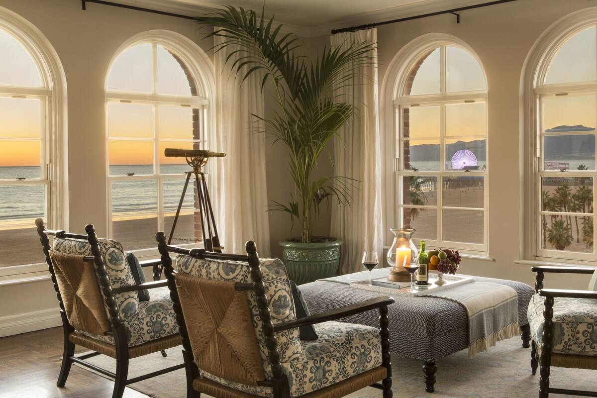 A room with a view of the beach, featuring a table with a candle, wine glasses, and a telescope.