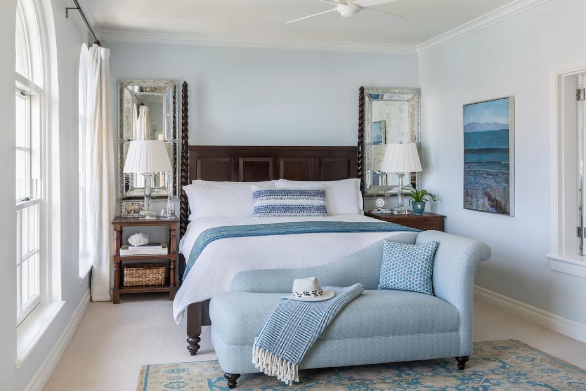 A bedroom with a large bed, two bedside tables with lamps, a chair, a rug, and a painting on the wall.