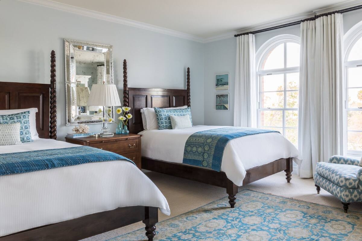 A bedroom with two beds, a nightstand, a dresser, a chair, and a large window with curtains.