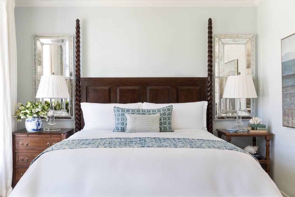 A neatly made bed with a white and blue patterned bedspread, flanked by two nightstands with lamps and decorative items.