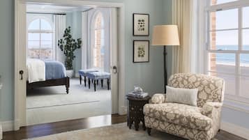 A bedroom with a bed, a chair, a lamp, and a view of the beach through a window.