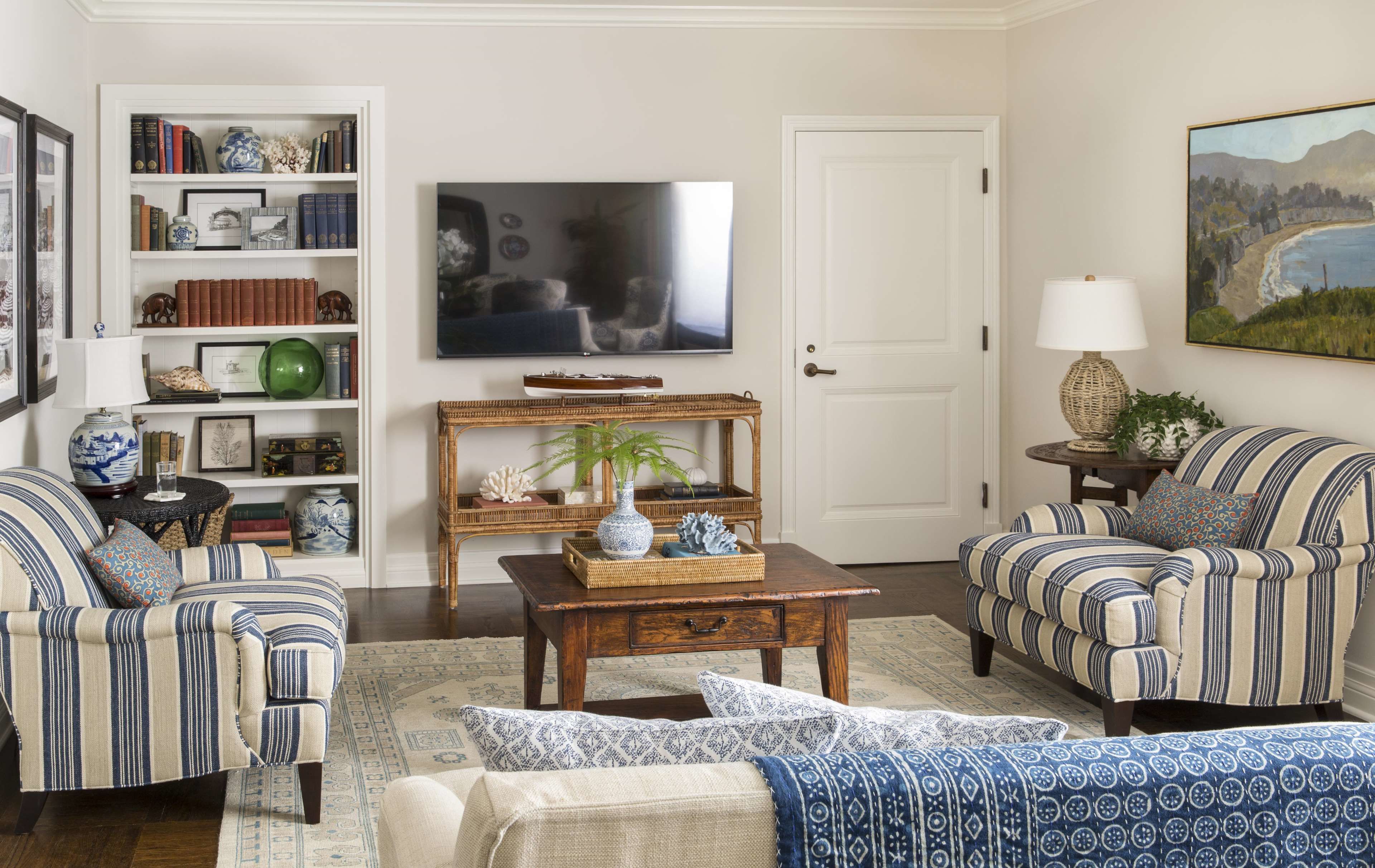 A living room with striped sofas, a coffee table, a bookshelf, a television, and a painting.
