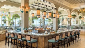 Uma área de bar com ilha central, banquetas, luminárias pendentes e vista para o oceano.