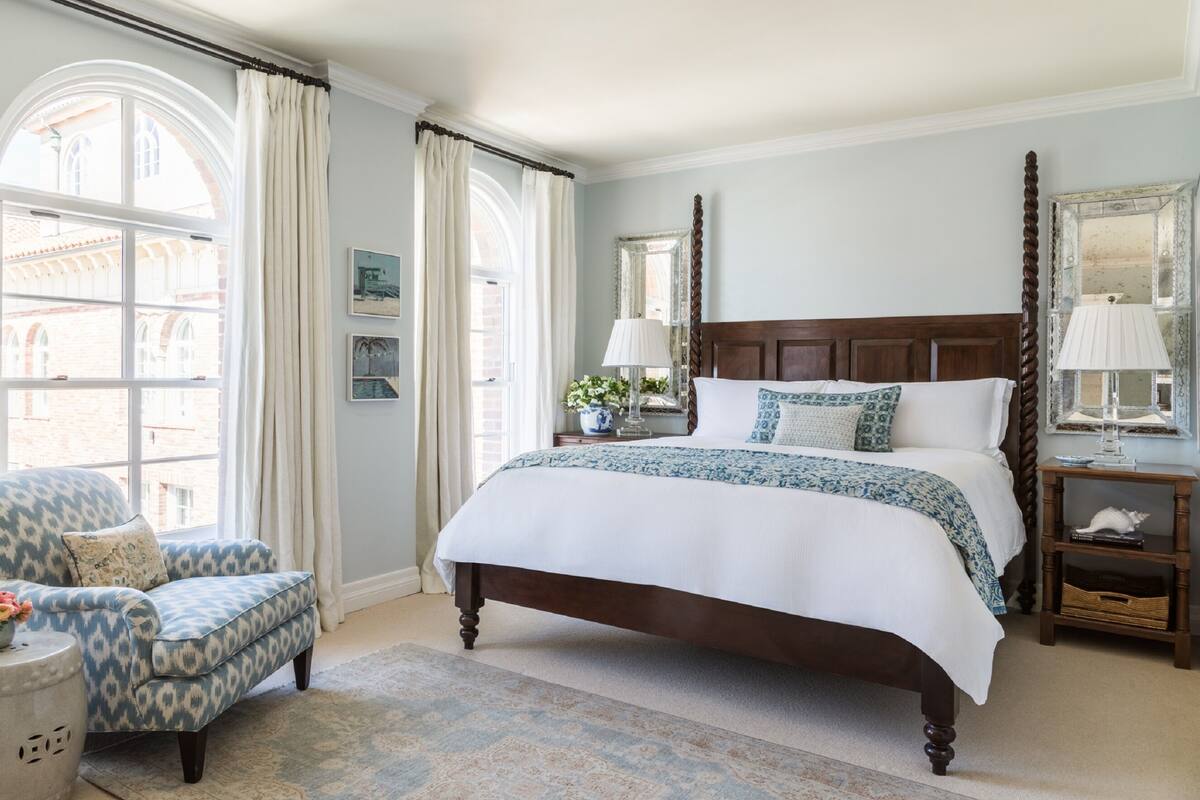 A bedroom with a large bed, a chair, a nightstand, and a window with curtains.